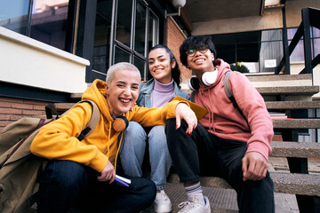 Group of three students outside the school looking at the camera. College classmates sitting on a staircase on campus university.