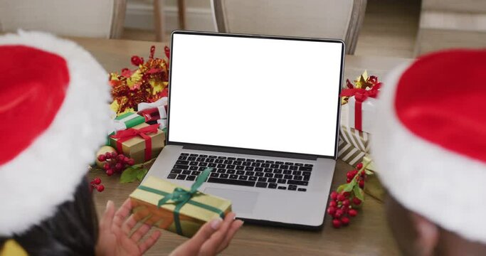 Animation of diverse couple in santa hats using laptop with blank screen at christmas