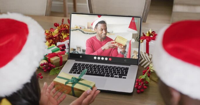 Animation of diverse couple in santa hats on laptop video call with man at christmas