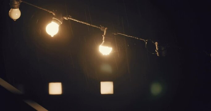 Heavy rain at night with decoration string lights hunging on backyard. static shot