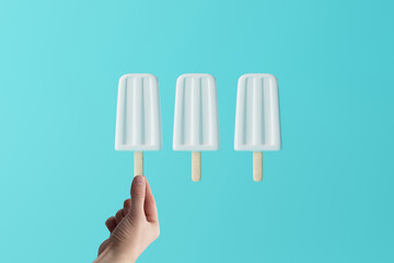 Hand holds white ice lolly on an blue pastel background. Concept of summer, vacation. Cooling down on warm days.