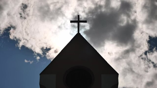 The silhouette of a Catholic church tower against a background of sun and clouds.