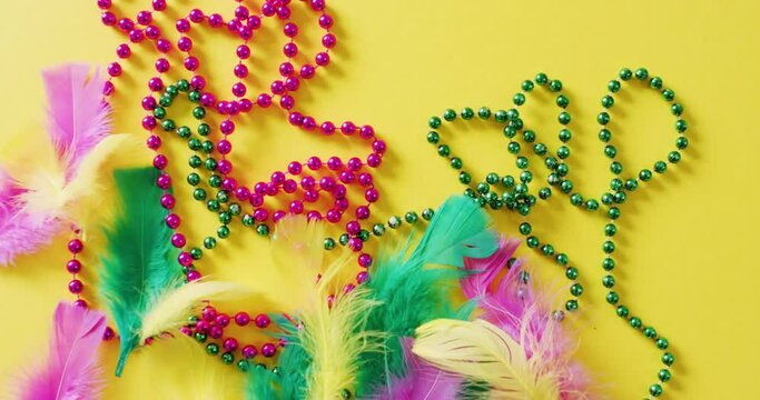 Video of pink and green mardi gras carnival beads and feathers on yellow background with copy space