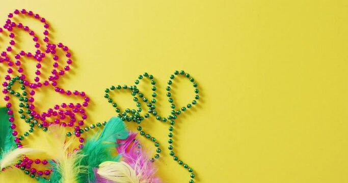 Video of pink and green mardi gras carnival beads and feathers on yellow background with copy space