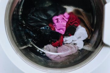 Wet dirty clothes are being washed, spinning in an electric washing machine inside with water behind a glass round porthole. Close-up photo, washing in the laundry, work.