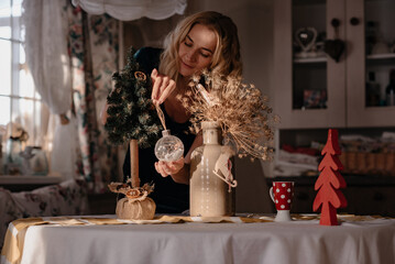 The girl is sitting in the kitchen drinking tea, the table is decorated with New Year's toys. beautiful blonde woman in her house decorates the house. Nice color photo.