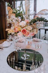 A beautiful bouquet, flowers from reeds, roses and wildflowers stand in a glass vase, set on a round table in a restaurant. Photography, wedding, decoration.