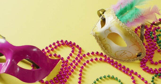 Video of two masquerade masks and carnival mardi gras beads on yellow background with copy space