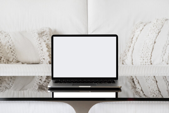 Laptop with white screen. Isolated laptop screen. Laptop view straight ahead. Laptop on a black glass table against a white sofa.