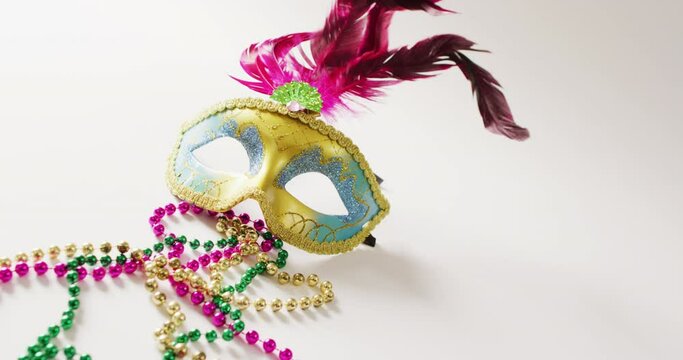 Video of masquerade mask with pink feathers and mardi gras beads on white background with copy space