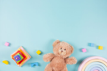 Baby kids educational toys frame background. Teddy bear, wooden stacking pyramide tower, toy rainbow and colorful blocks on light blue background. Top view, flat lay