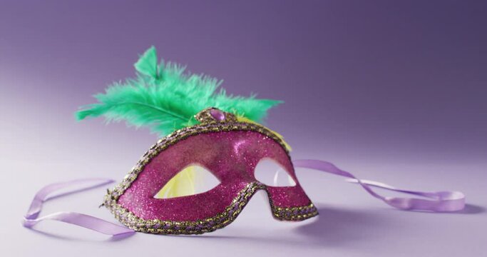 Video of pink carnival masquerade mask with green feathers on white and purple background