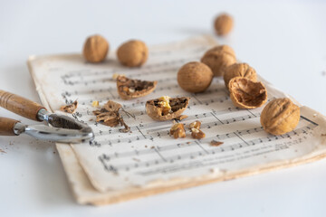 Nutcracker with walnuts in a rusty tin box on music paper on a white table. Place for your text
