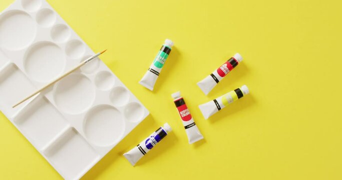 Video of tubes of water colour paint, paintbrush and palette on yellow background with copy space