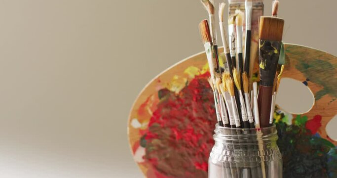 Video of a collection of paintbrushes in a jar and used palette on grey background with copy space