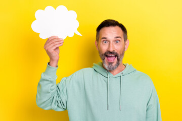 Photo of overjoyed excited mature aged man wear khaki sweatshirt hold paper bubble cloud empty space opinion isolated on yellow color background