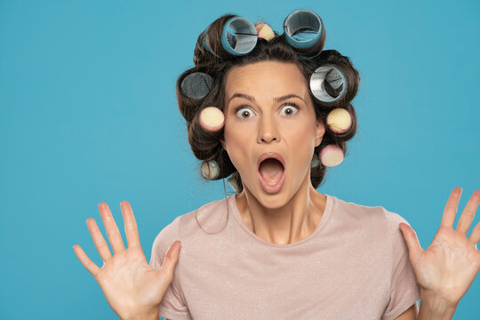 Beautiful terrified woman with hair curlers posing on a blue background