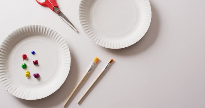 Video of paper plates with paint, paintbrushes and scissors on white background with copy space