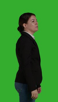 Vertical video: Profile close up of company employee raising hand and waving to call someone over, standing on isolated greenscreen backdrop. Young female worker asking and calling people to discuss