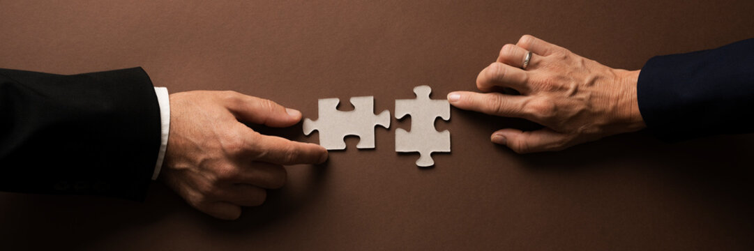 Wide view image of businessman and businesswoman hands joining two blank matching puzzle pieces