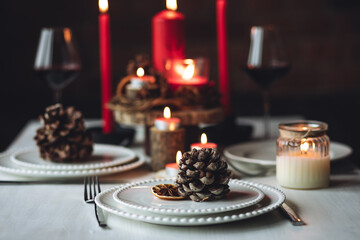Rustic table decor for Christmas or New Year family dinner. Centrepiece with red candle, dry orange, cone, cinnamon, anise. Zero waste eco-friendly home. Cozy atmosphere, dark background. Close up