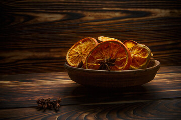 natural orange chips in a plate and anise on a wooden table under the light of an evening lamp. selective focus 