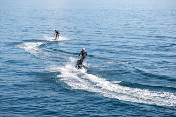 Two men ride on an electric surfboard. Pair surf on an electric board