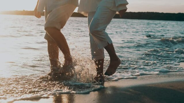 Couple of old mature people walking on the sand together and having fun on the sand of the beach enjoying and living the moment. Two cute seniors in love having fun. Barefoot walking on the water