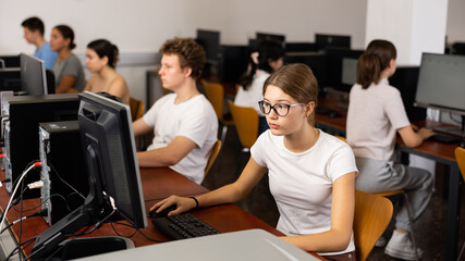 Fototapeta premium Positive female teenager in glasses learning computer science while she is using a PC in the computer classroom