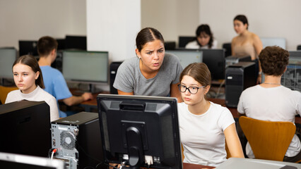 Fototapeta premium Young female teacher working with schoolgirl in computer class of school library