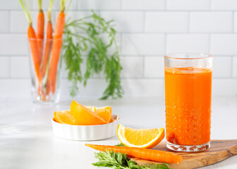 Glass of fresh organic homemade carrot-orange juice with orange slices in a bright kitchen counter scene with copy space