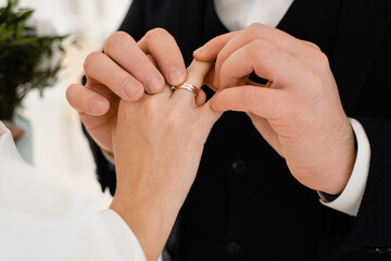 Groom puts wedding ring on top of engagement ring for bride