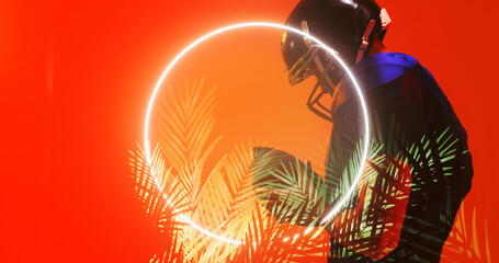 American football player wearing helmet and holding ball by illuminated circle and plants