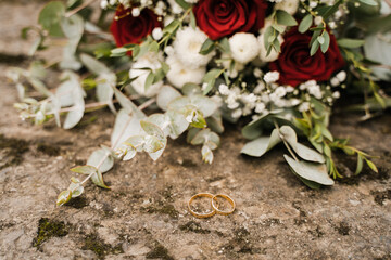 wedding gold rings and a bouquet lie on a stone