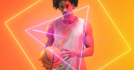 Naklejka premium Serious biracial basketball player with ball standing over illuminated multiple geometric shapes