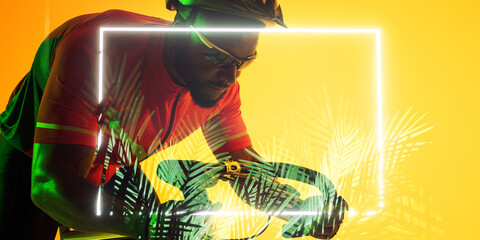 African american male cyclist riding bike by illuminated rectangle and plants on yellow background