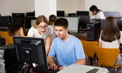 Fototapeta premium Teenager girl helps friend solve problem on computer in a school class