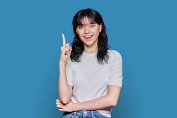 Happy young woman showing index finger up, over blue background