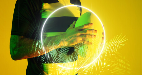 Midsection of caucasian rugby player holding ball by circle and plants over yellow background