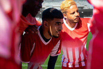 Multiracial young male soccer players huddling and planning match strategy at stadium on sunny day