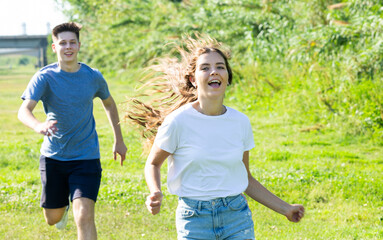 Obraz premium Laughing teenagers playing outdoors funning at grass on summer day
