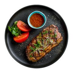 juicy Striploin Steak with tomato sauce and vegetables on black plate top view isolated on white background