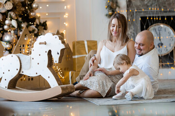 Obraz na płótnie Canvas Merry Christmas! Mom, dad and little daughter dressed up at a beautiful Christmas tree in the living room. Family morning on Christmas eve, waiting for gifts. The concept of family unity.