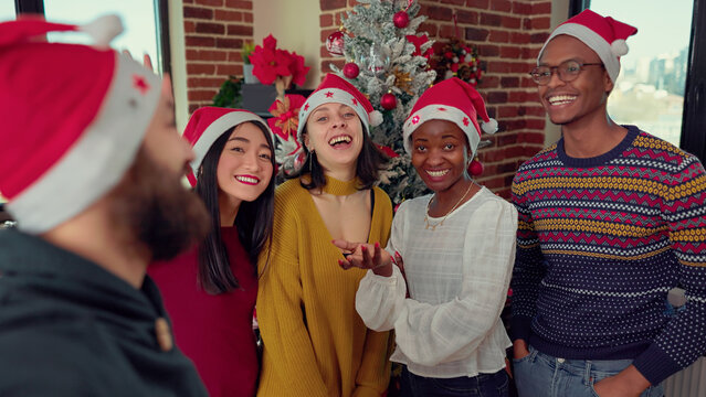 Multiethnic group of employee recording video in festive office, filming on camera during christmas eve party celebration. Cheerful people taking pictures and having fun on xmas holiday.