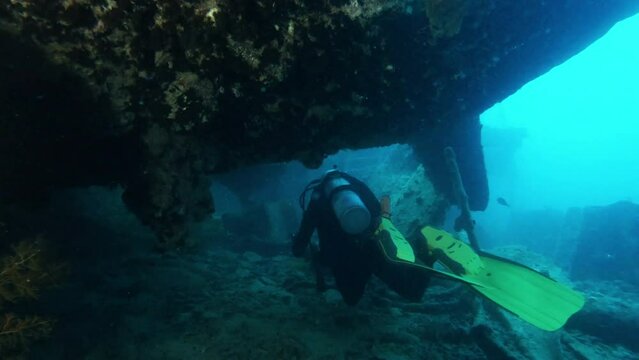 Diver exploring sunken ship underwater, shining with flashlight, back view tracking shot. Ocean bottom scuba diving, old vessel wreck undersea