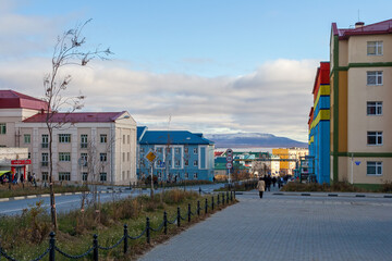 Fototapeta na wymiar Anadyr, Chukotka, Russia. Autumn view of the street of a well-maintained northern city located in the Arctic. People walk along the sidewalk past colorful buildings.