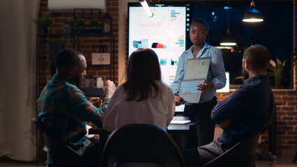 African american employee presenting report, showing charts on laptop screen. Company research statistics presentation, diverse team discussing analytics, planning sales strategy