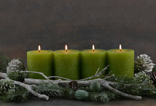 Adventsdeko aus Naturmaterial. Dekoration zum vierten Advent. Vier grüne brennende Kerzen mit Zweigen und Zapfen.