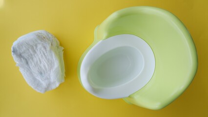 Diapers and baby green plastic potty on yellow background, top view