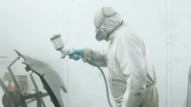 Close-up shot of a service station, painting shop working progress. Detailed view of a worker in white, protective, suit. High quality 4k footage